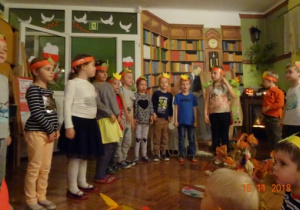 Dzieci w opaskach na głowie recytują wiersz. Na środku stoi jesienny kosz.
